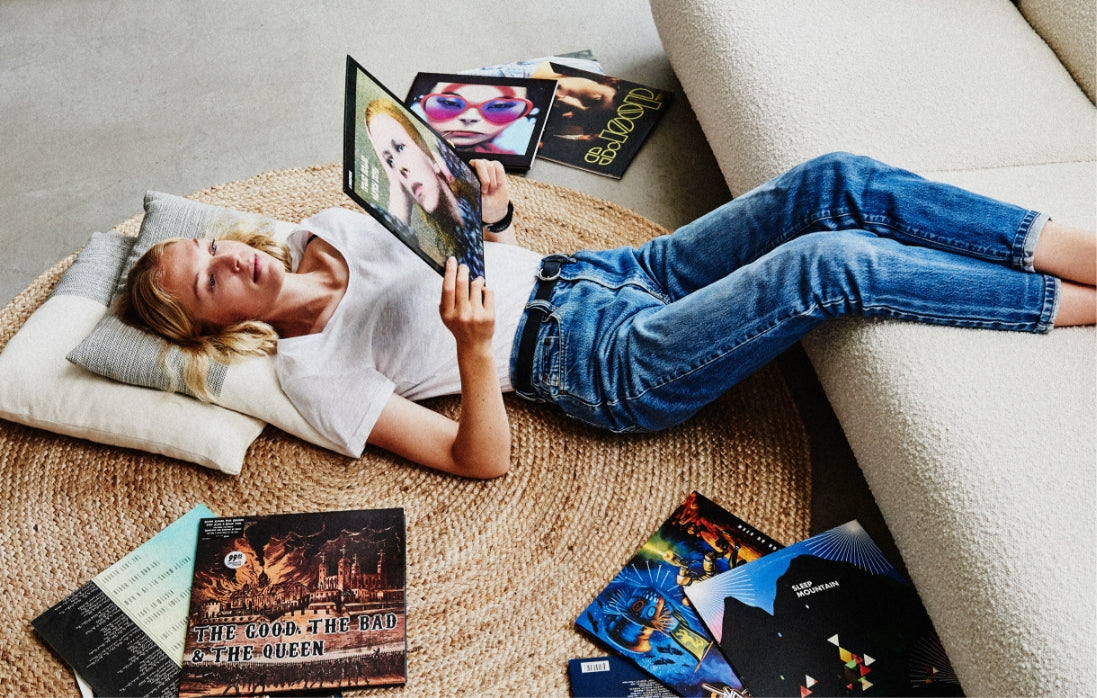 A woman laying on the floor looking at a record, with albums beside her